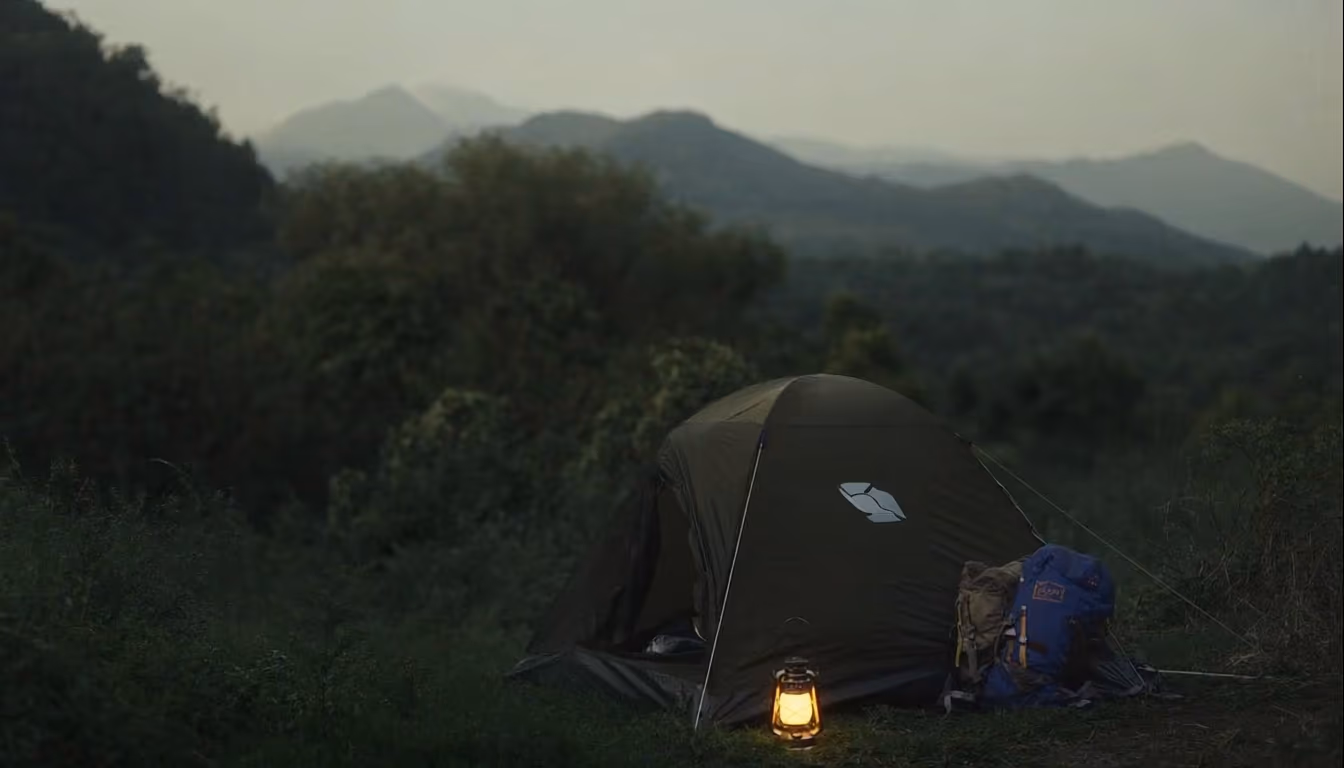 Camping tent and lantern at dusk with misty mountains in background